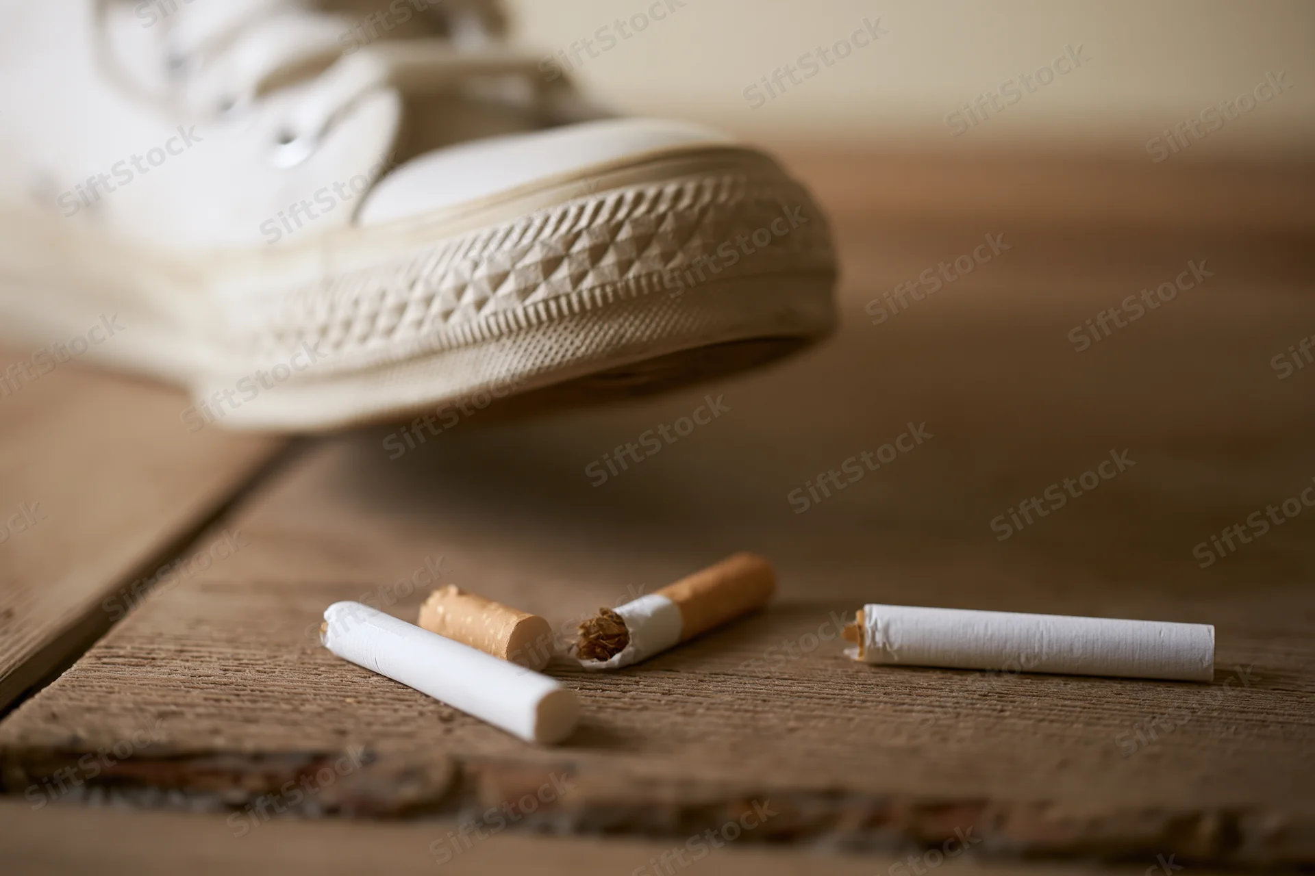 White canvas sneaker sole hovering above discarded cigarettes on wooden floor