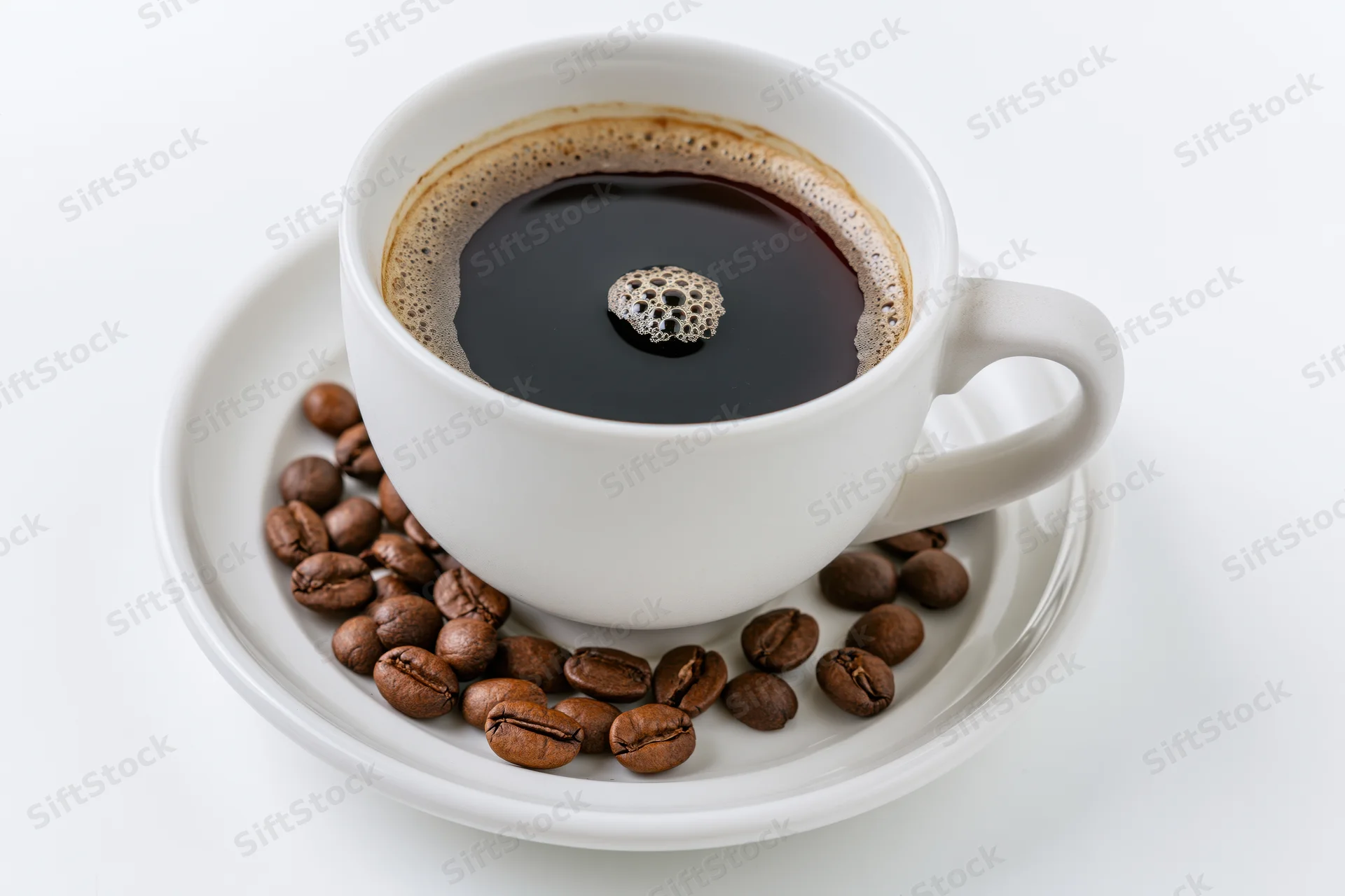 White ceramic coffee cup filled with black coffee and foam bubble on saucer with roasted beans around it