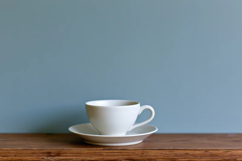 White ceramic coffee cup on matching saucer resting on wooden table against blue wall