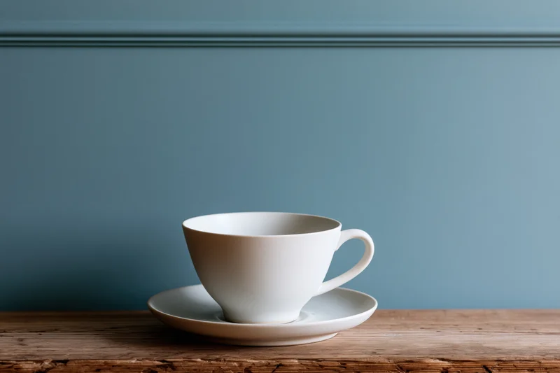 White ceramic coffee cup on matching saucer resting on wooden table against blue wall