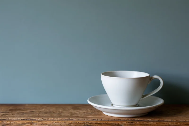 White ceramic coffee cup on matching saucer resting on wooden table
