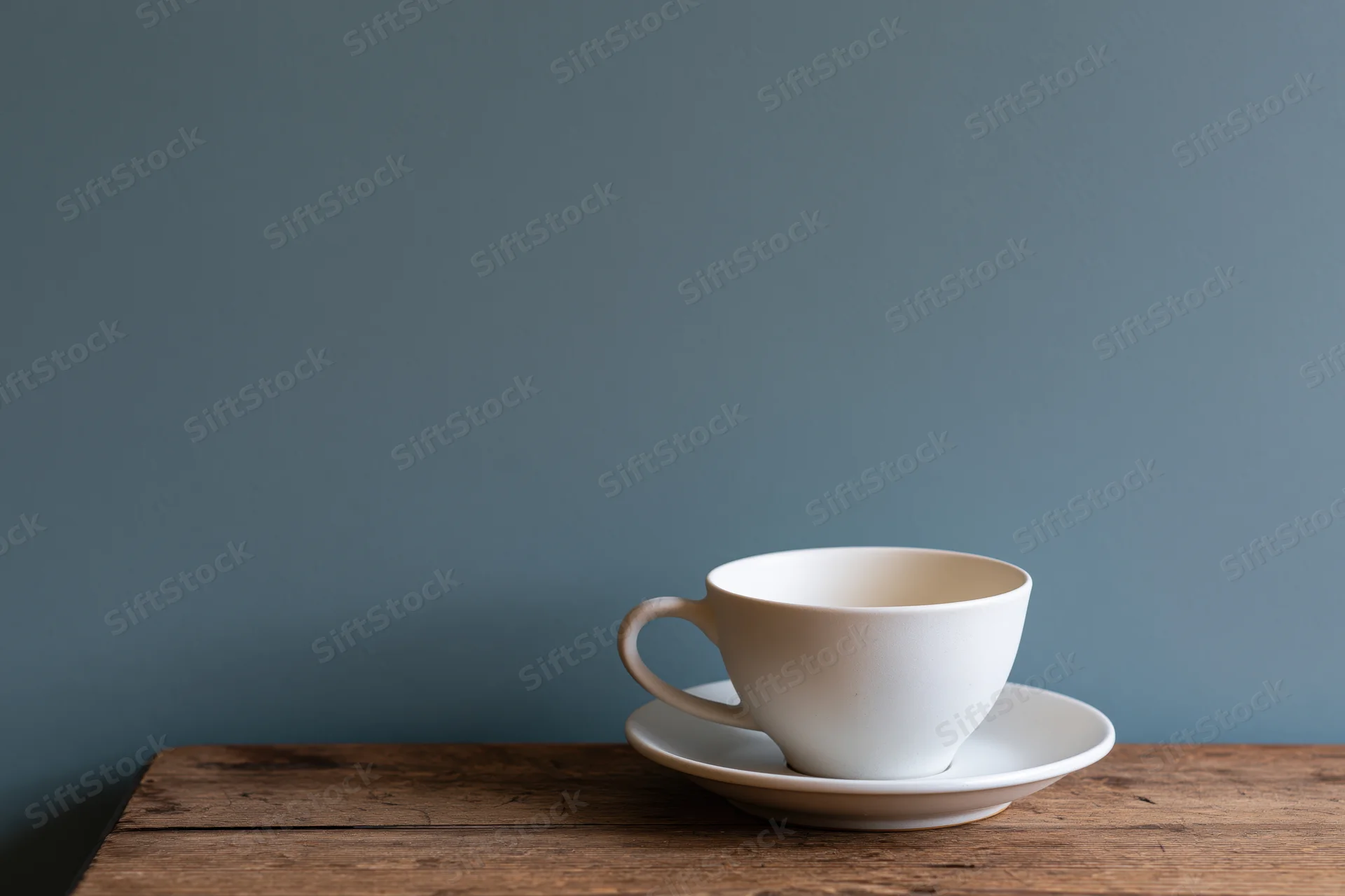 White ceramic coffee cup on matching saucer resting on wooden table against blue wall