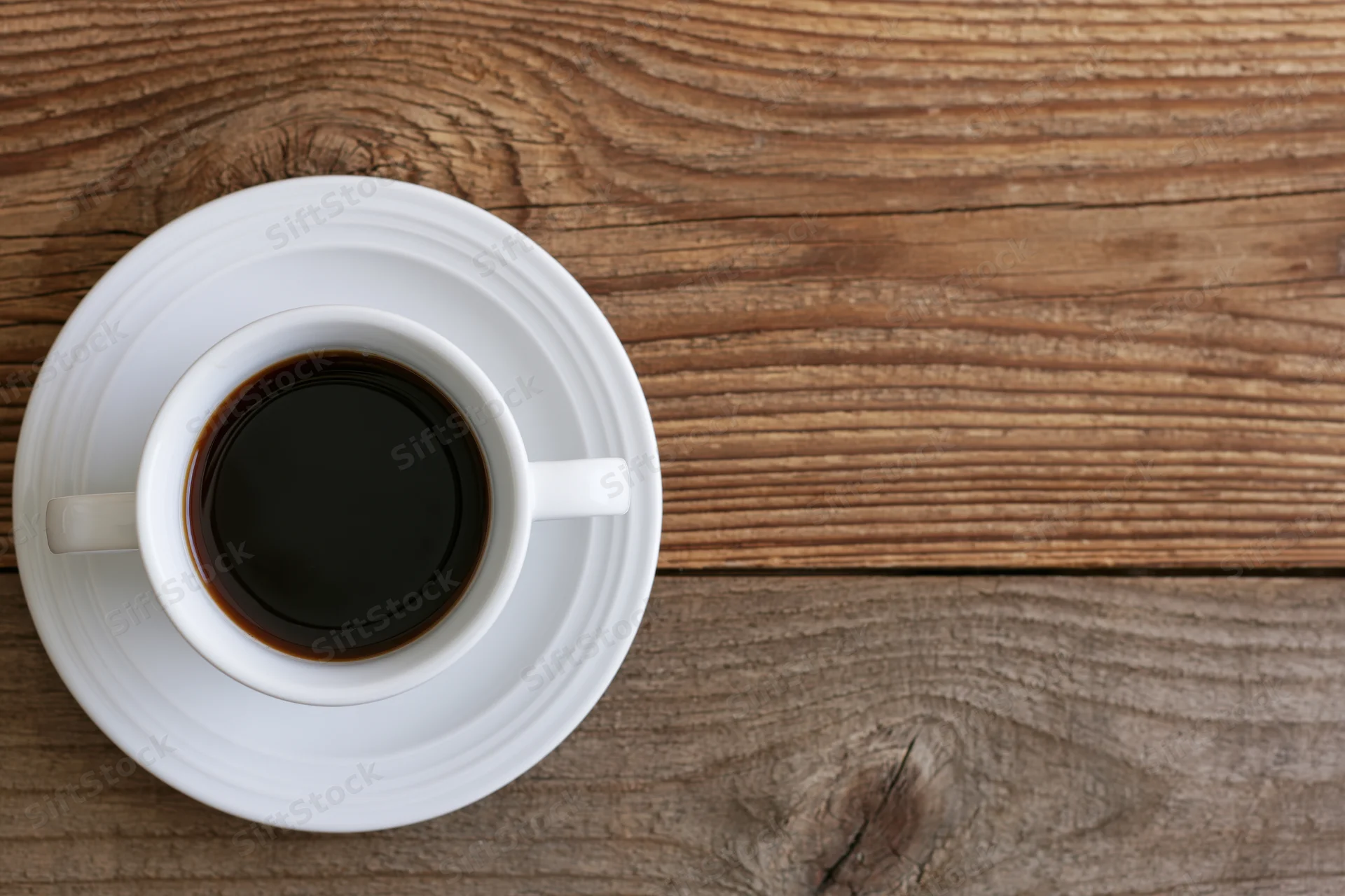 White ceramic coffee cup on matching saucer on wooden table top view