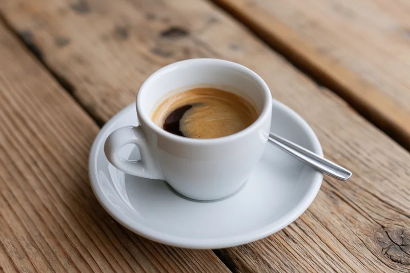 White ceramic espresso cup with foam on wooden table