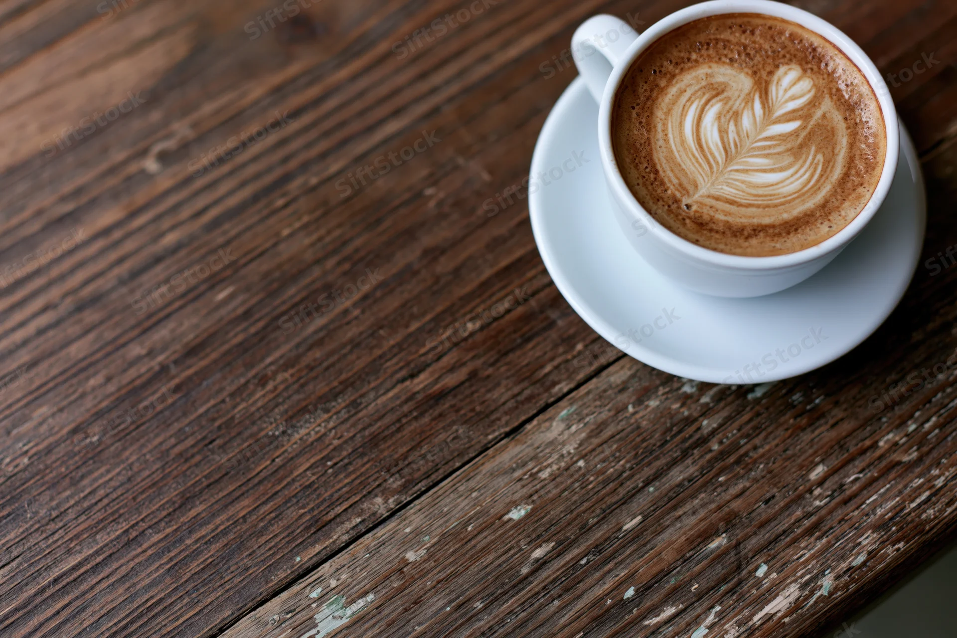 White ceramic cup of latte with leaf latte art on a rustic wooden table