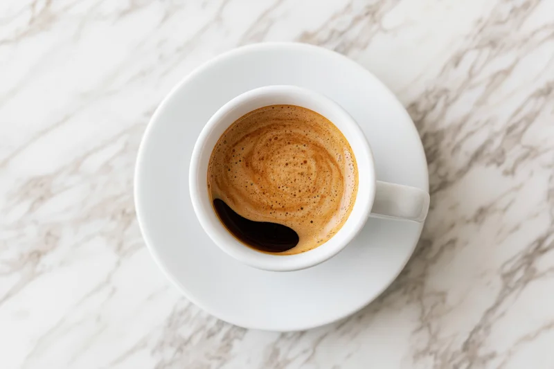 White ceramic espresso cup with crema and dark swirl on marble tabletop