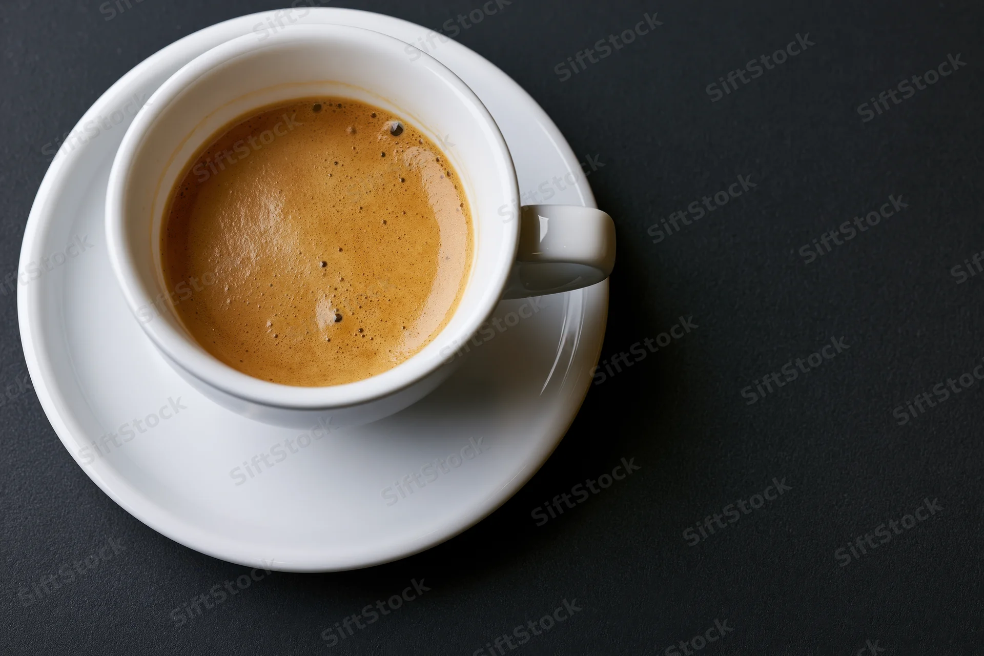 White ceramic espresso cup with crema on saucer on dark surface