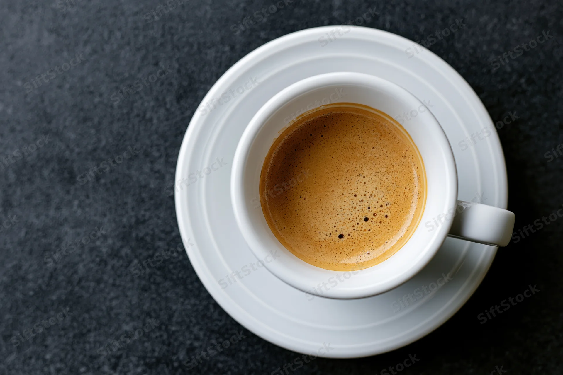 White ceramic espresso cup with crema on saucer on dark surface, overhead view