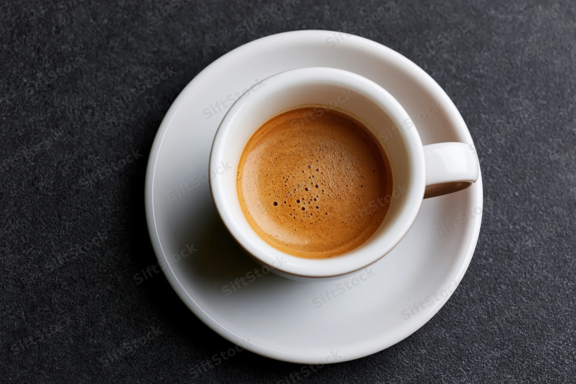 White ceramic espresso cup filled with crema on a saucer on dark surface