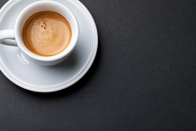 White ceramic espresso cup with crema on saucer on dark surface