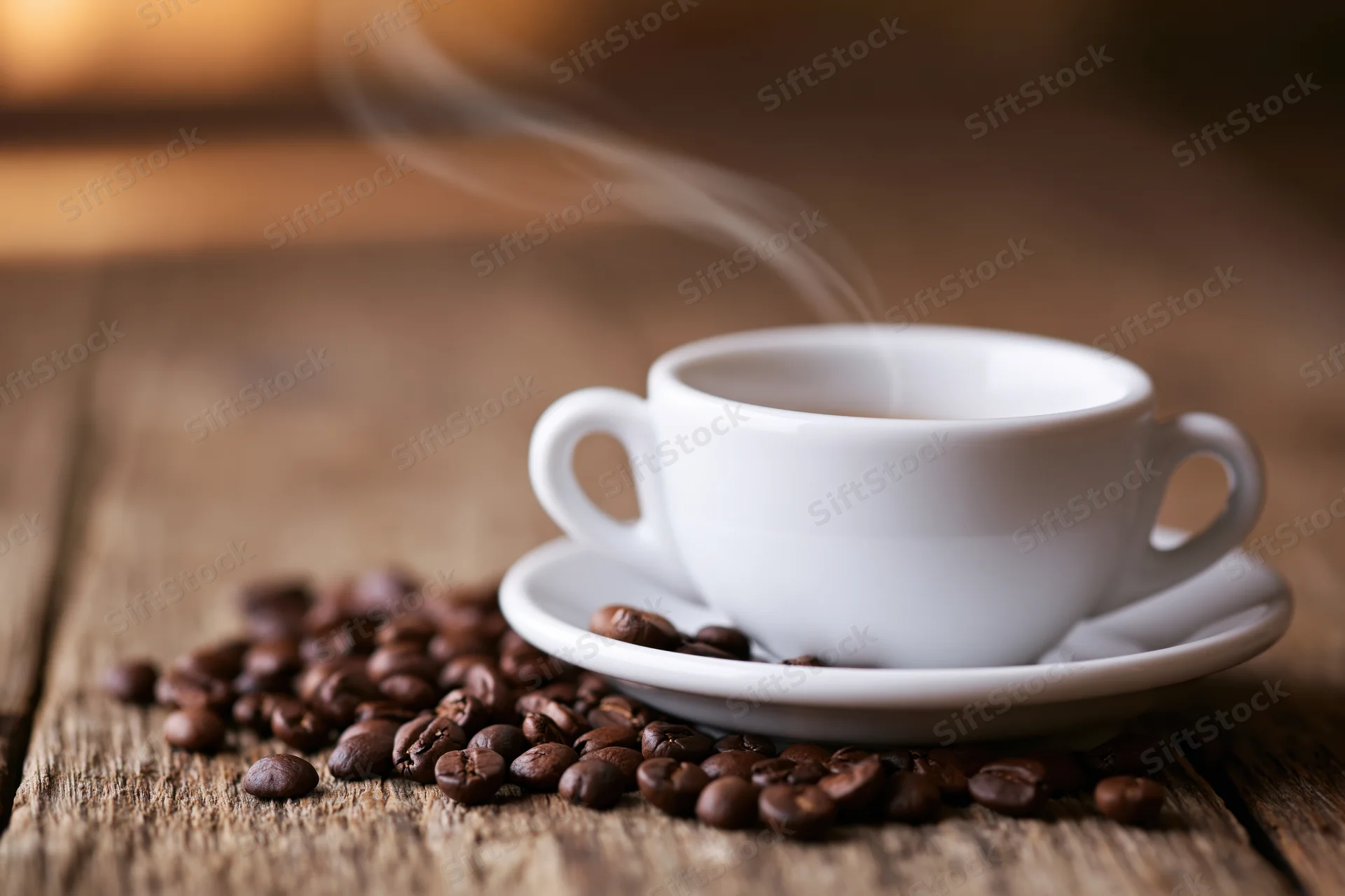White ceramic espresso cup with steam on a wooden table surrounded by coffee beans