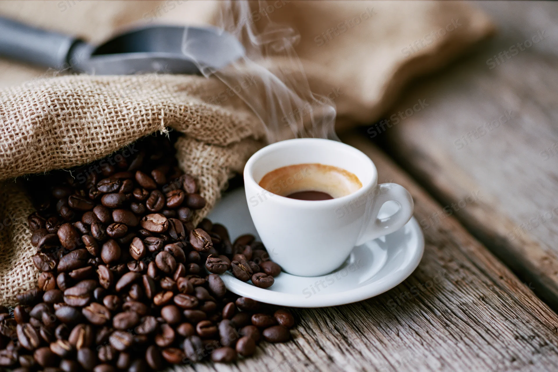 Steaming espresso cup on a saucer beside roasted coffee beans spilling from a burlap sack on a wooden table