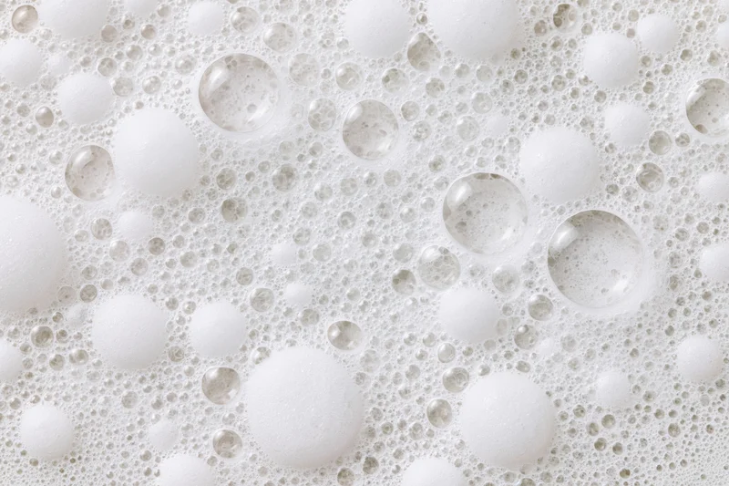 Closeup of white soap foam and bubbles scattered across a wet surface