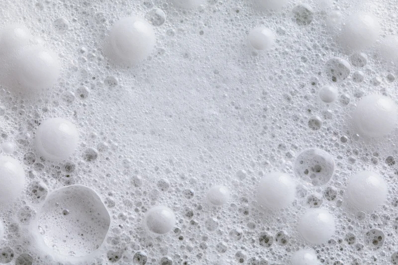 Closeup of white soap foam and bubbles scattered across a wet surface
