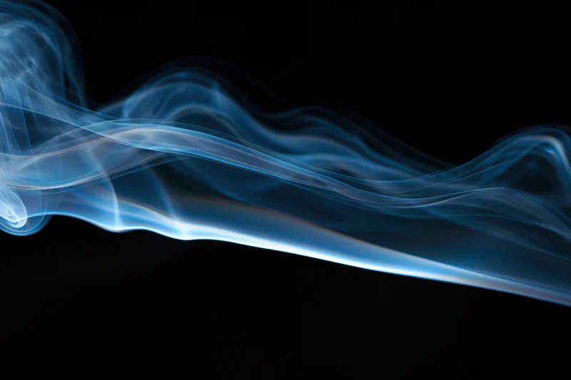 Wispy blue smoke plume drifting and curling in mid-air against black background