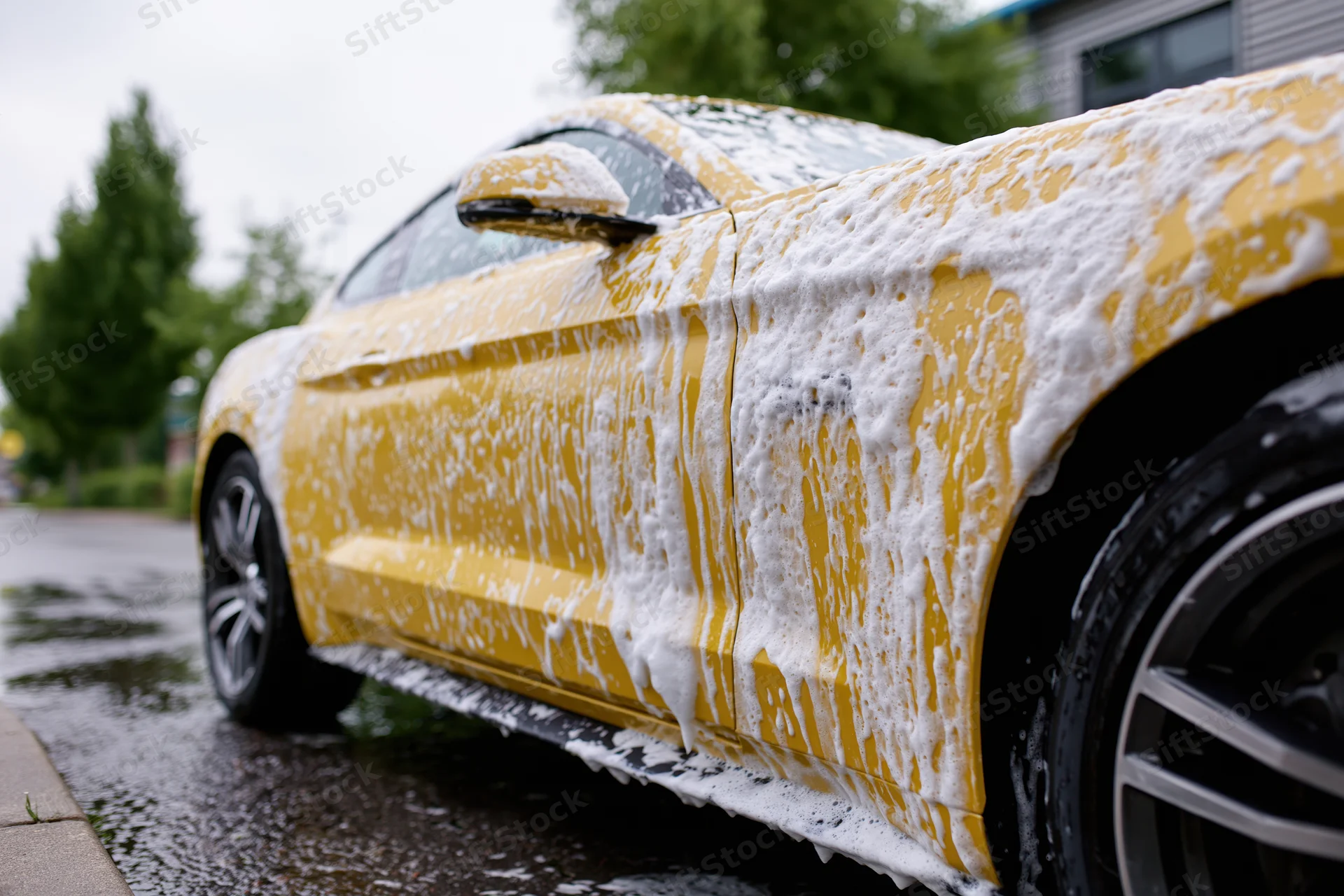 Yellow ford mustang coupe covered in thick white soap foam during outdoor car wash on wet driveway