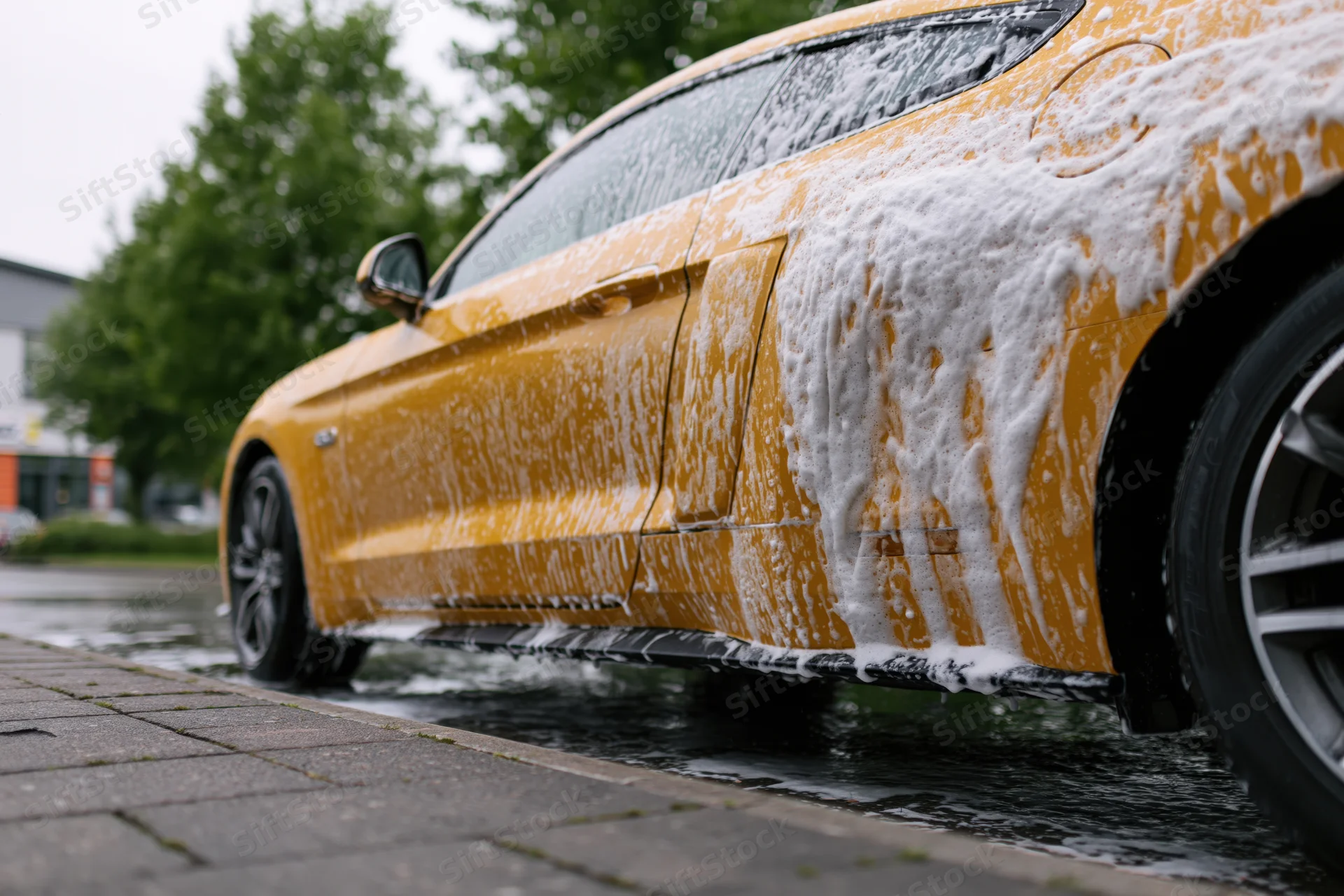 Yellow ford mustang coupe covered in thick white soap foam during outdoor car wash on wet pavement