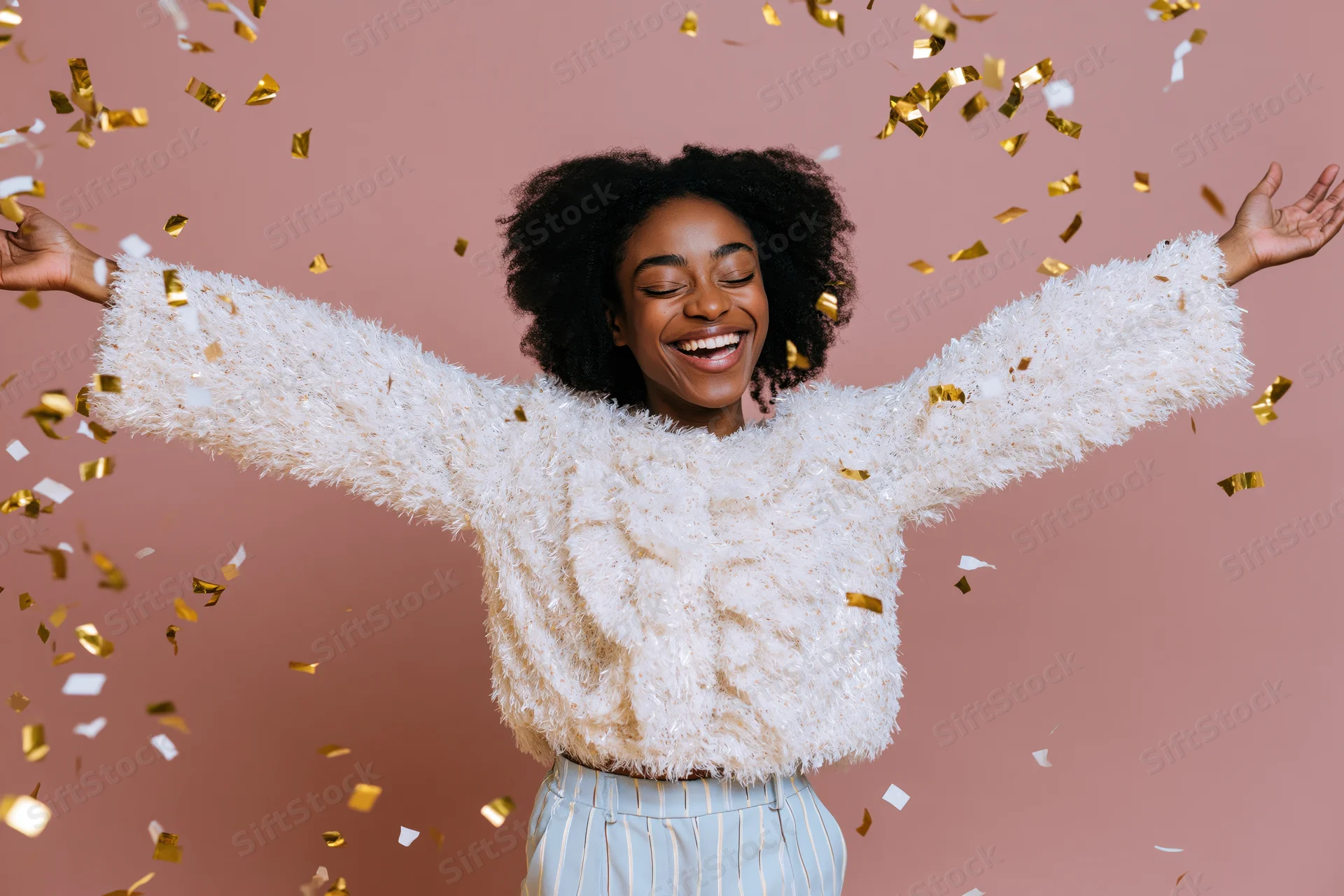 Young black woman laughing with arms open amidst falling gold confetti in studio setting