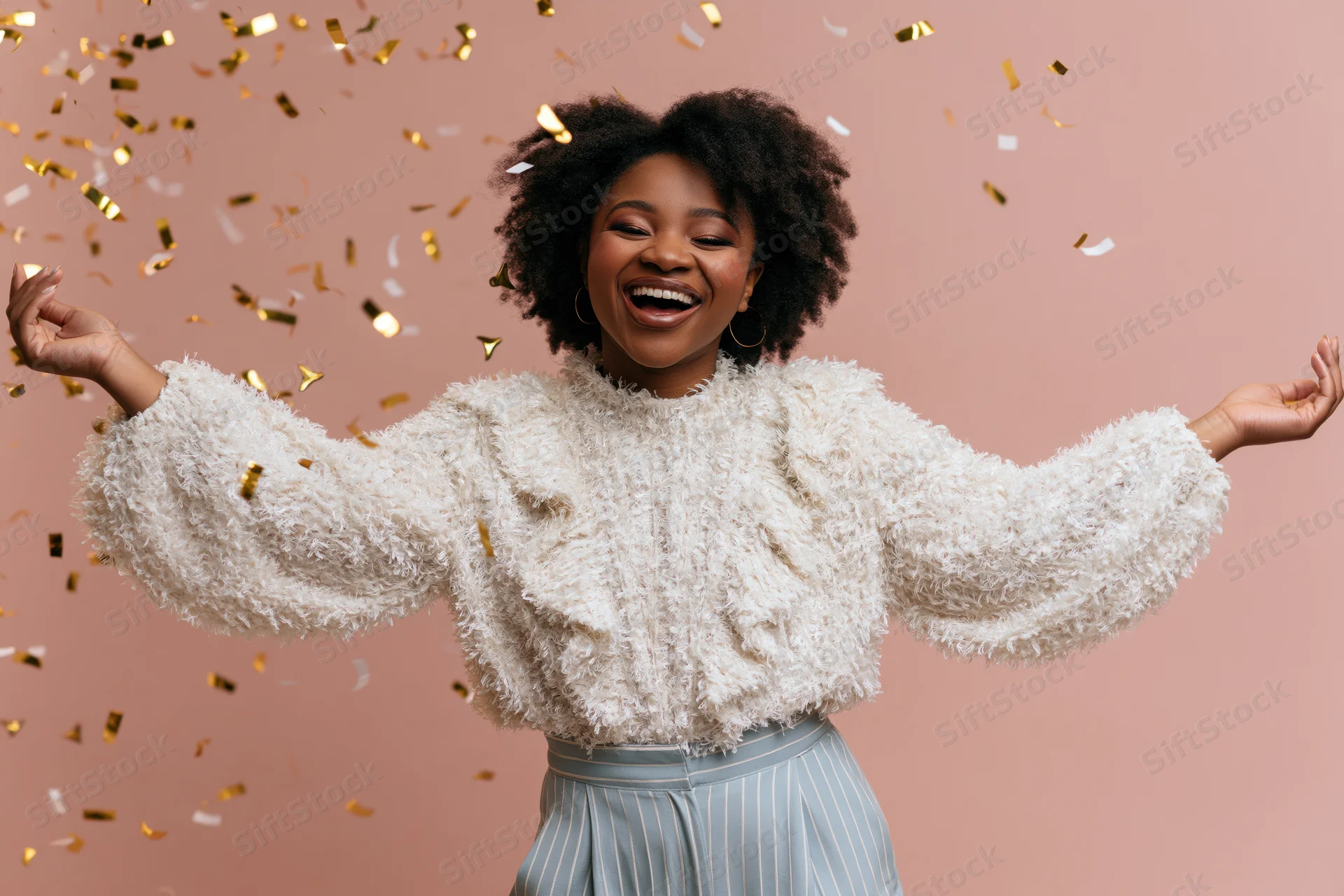 Young black woman laughing with arms spread amidst falling confetti against pink background