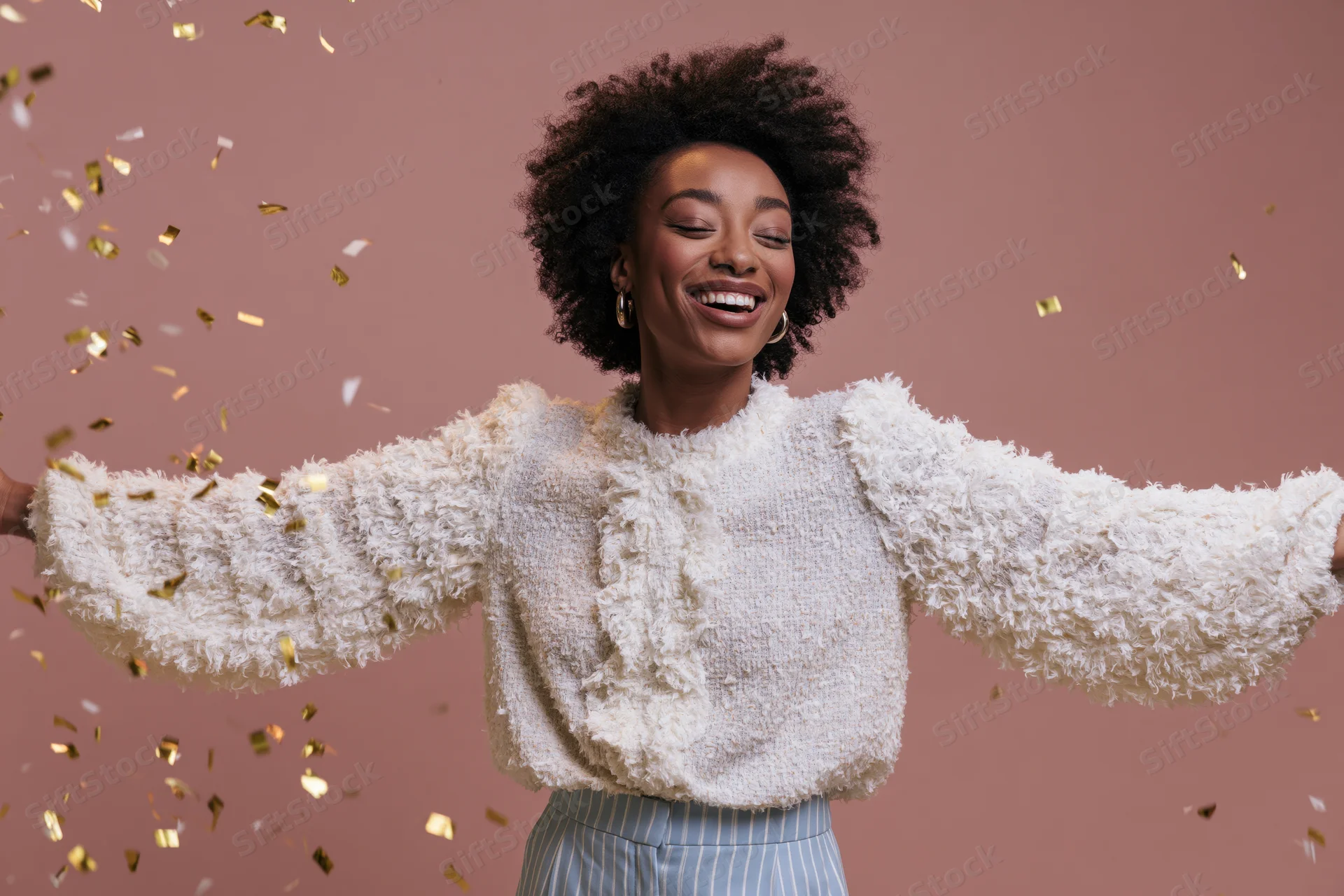 Young black woman laughing with arms spread amidst falling gold confetti in studio setting