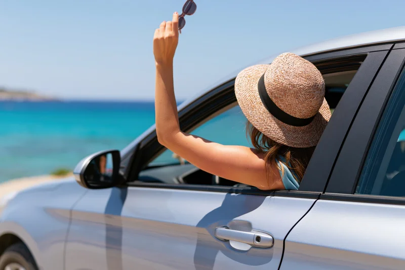 Woman leaning out of car window holding sunglasses by the sea
