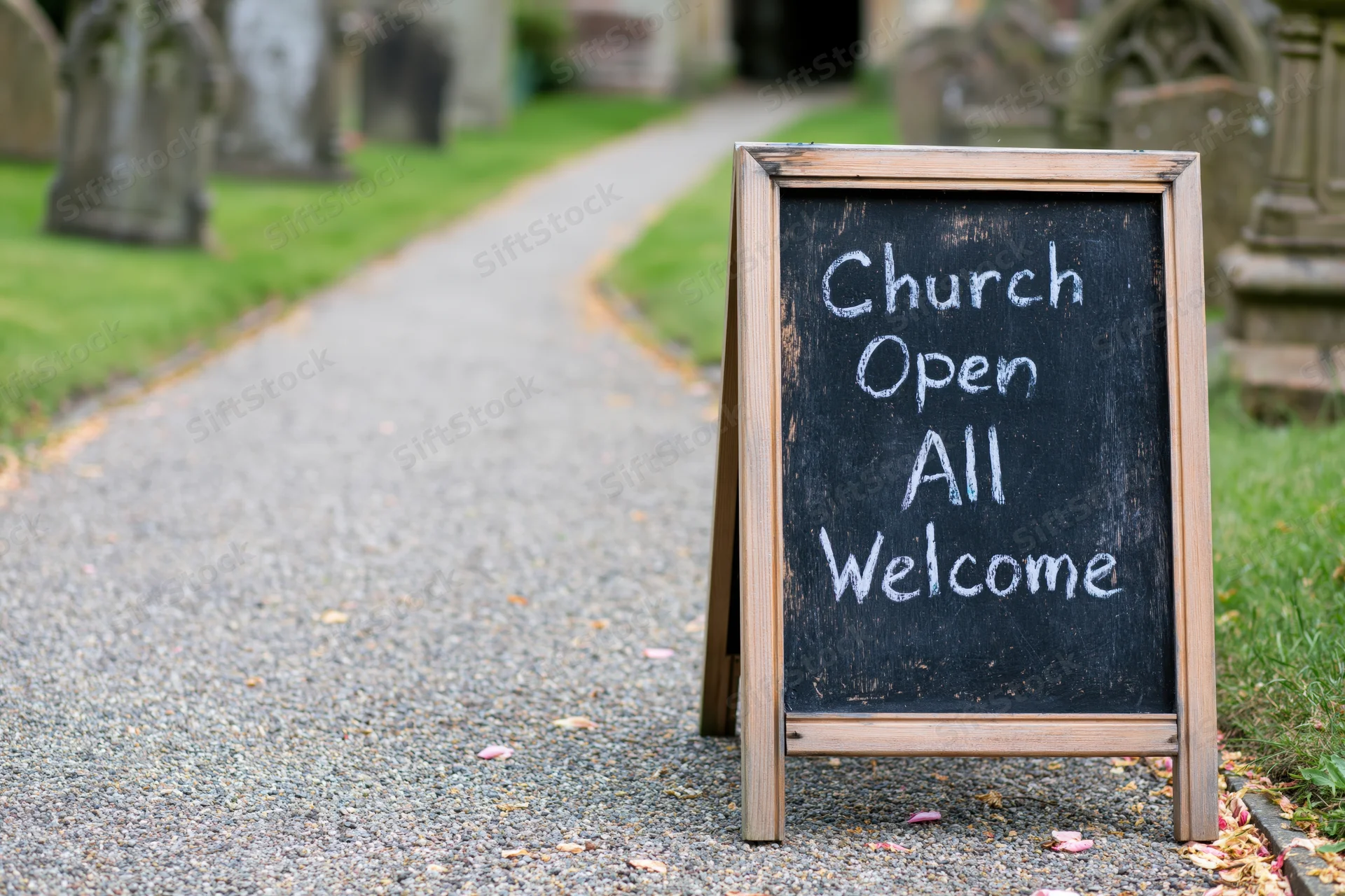 Aframe chalkboard sign reading church open all welcome on gravel path near graveyard