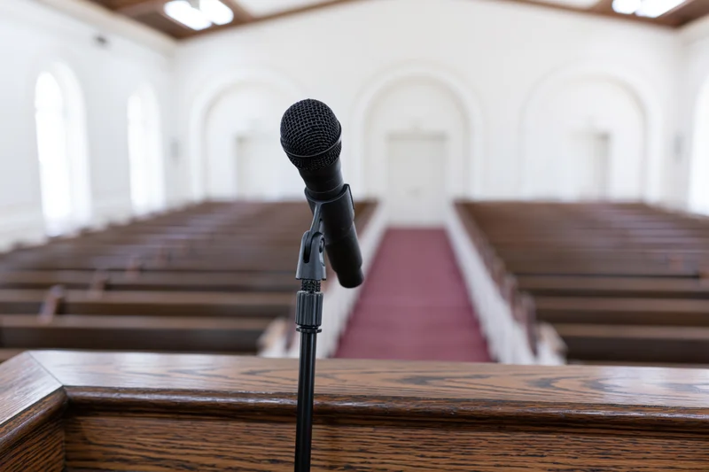 Black microphone on wooden pulpit in front of church pews and red carpeted aisle