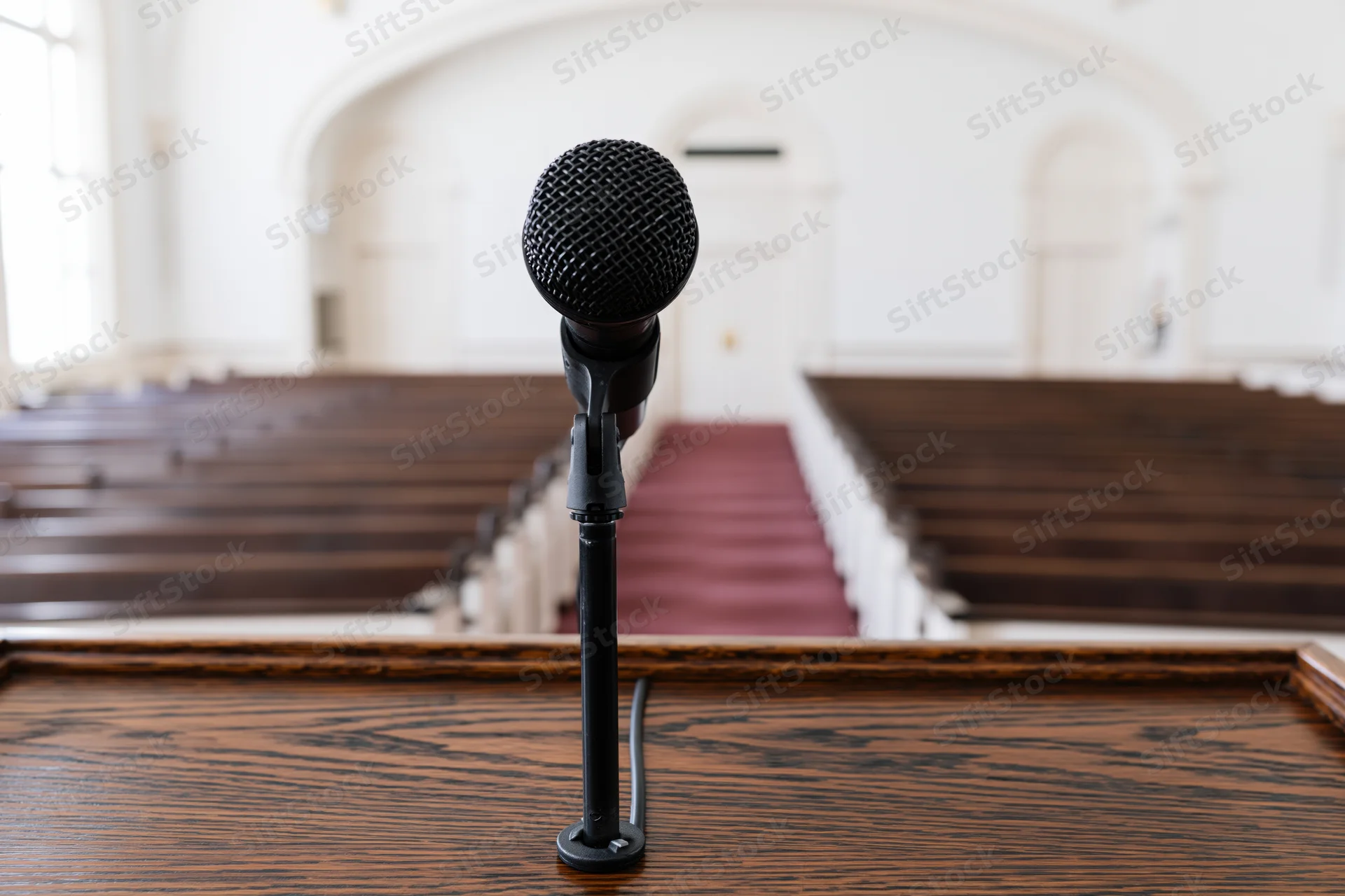 Black microphone on wooden podium in front of church pews and aisle
