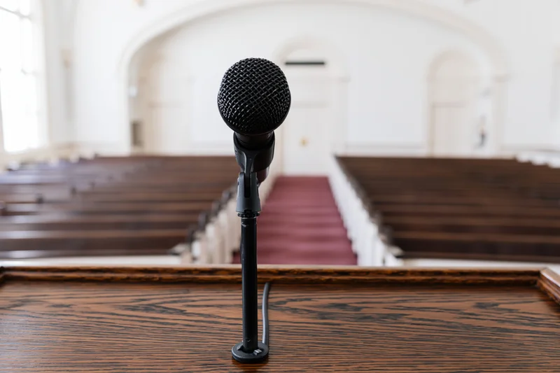 Black microphone on wooden podium in front of church pews and aisle