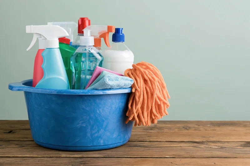 Blue plastic bucket filled with cleaning supplies and mop on wooden table