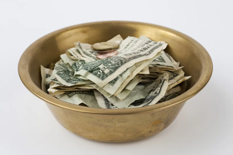 Brass bowl filled with us dollar bills and coins on white background