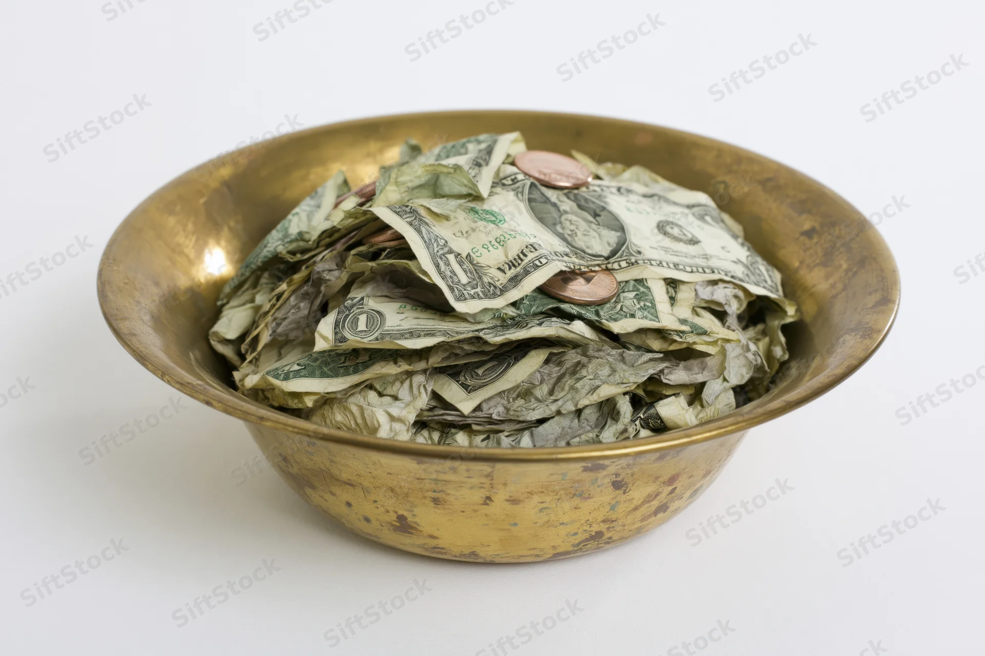 Brass bowl filled with crumpled us dollar bills and coins on white background