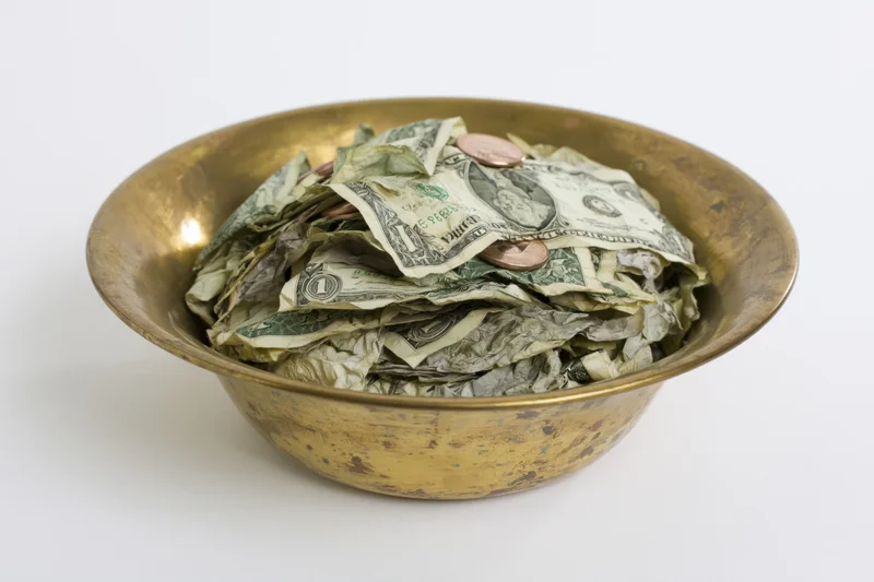 Brass bowl filled with crumpled us dollar bills and coins on white background