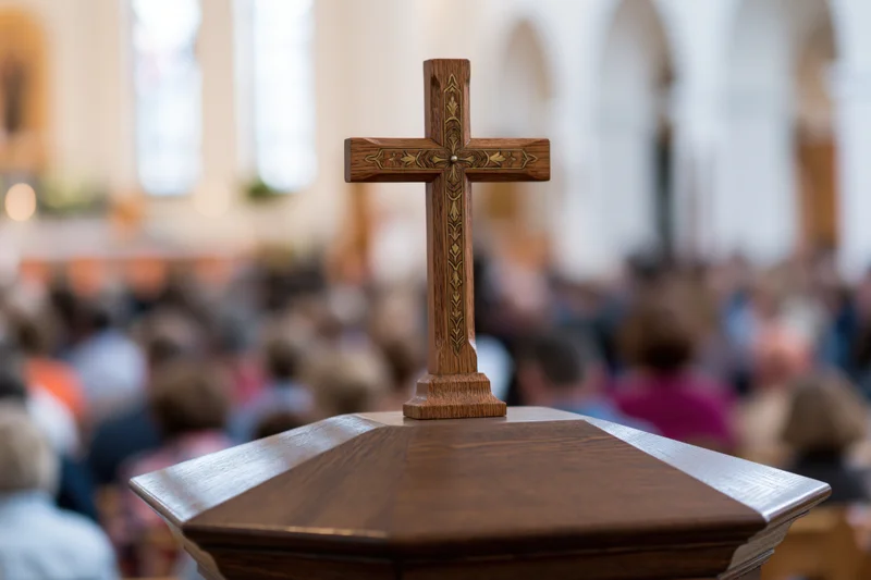 Carved wooden cross with brass inlay on pulpit in church during service with congregation in background