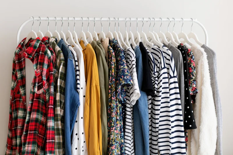 Assorted casual garments hanging on a white clothing rack against a plain wall