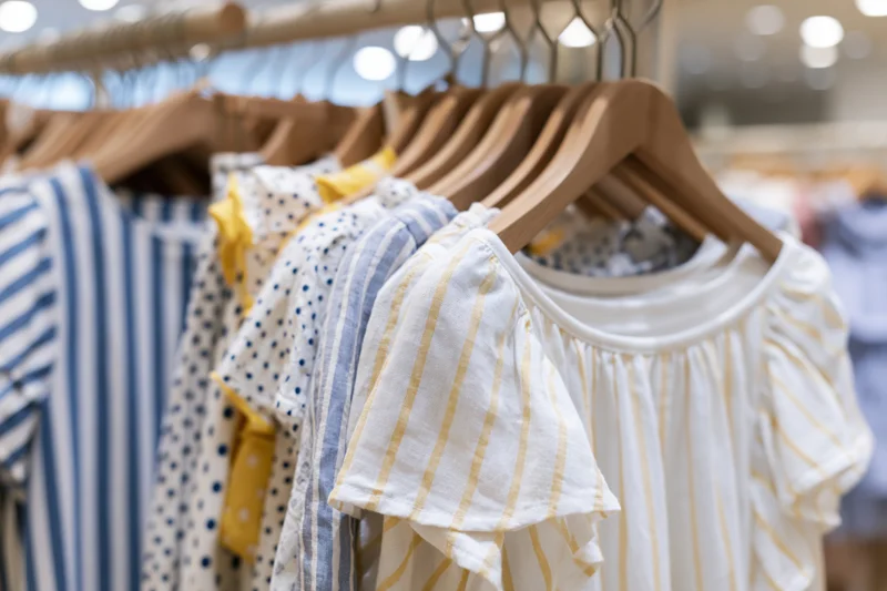 Women's blouses and ruffled dresses hanging on a wooden rack in a retail store