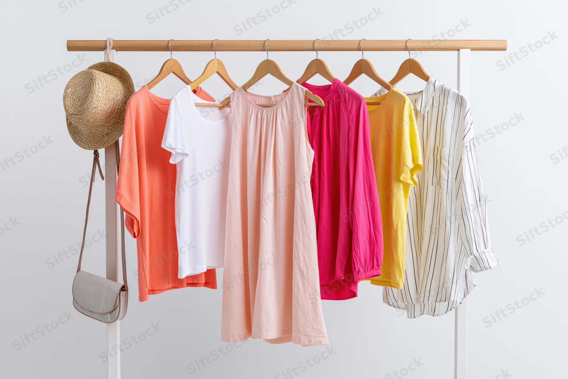 Women's summer clothing on a wooden rack with straw hat and crossbody bag