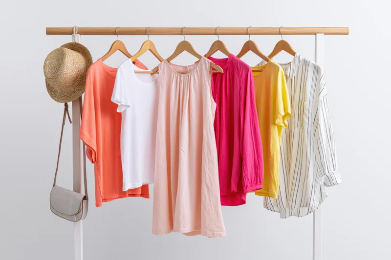 Women's summer clothing on a wooden rack with straw hat and crossbody bag