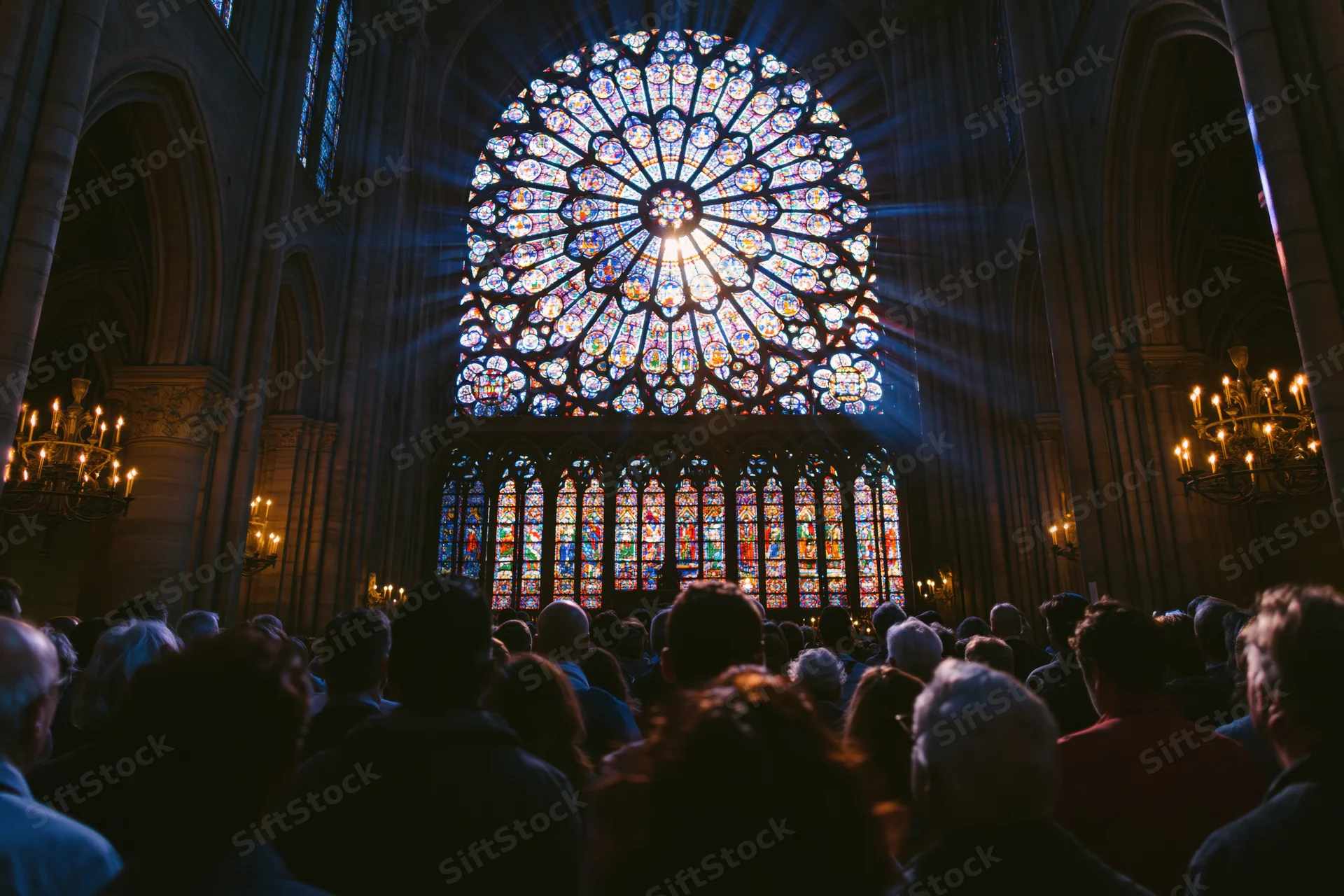 Crowd of visitors in silhouette facing a large stained glass rose window inside a gothic cathedral