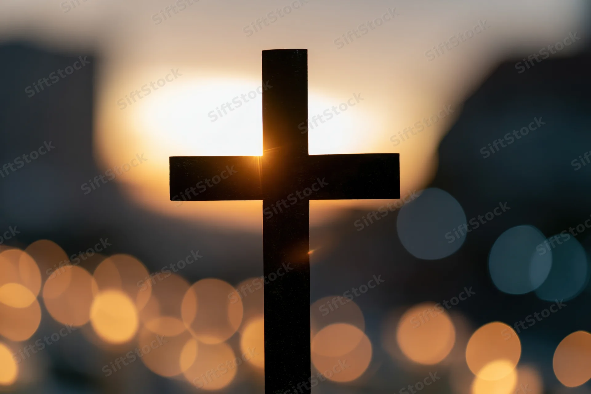 Silhouetted christian cross against a glowing sunset sky with blurred city lights below