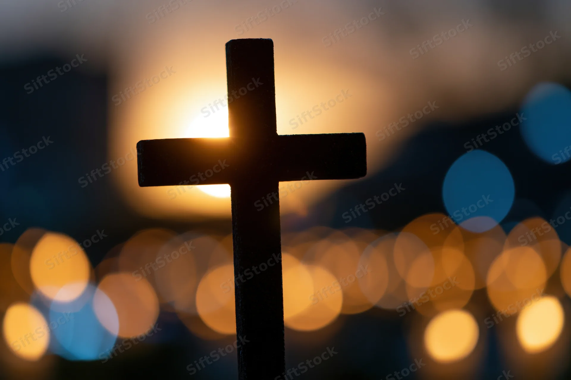 Silhouetted christian cross against a glowing sunset with blurred city lights in the background