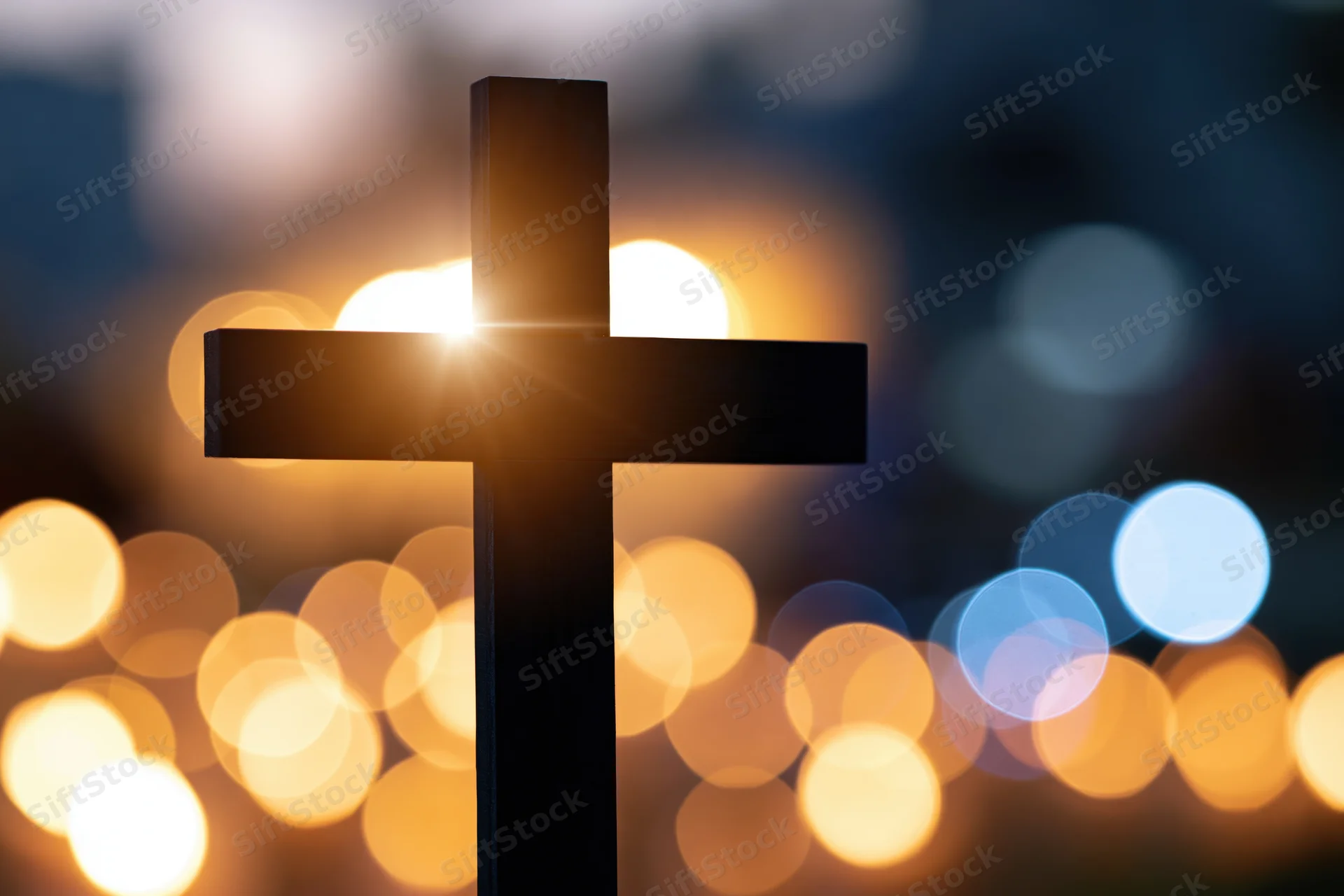 Dark silhouetted christian cross against glowing bokeh lights at night