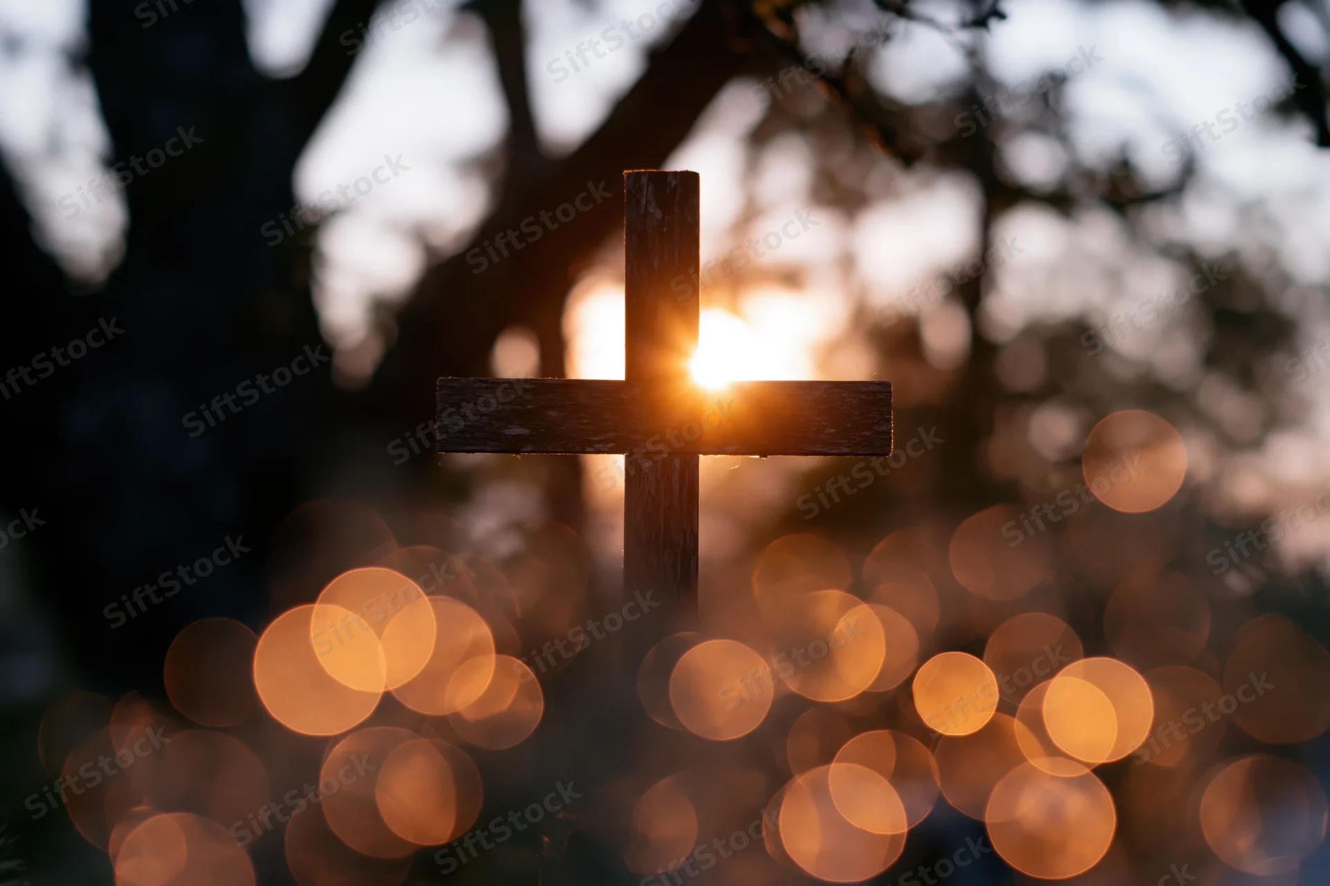 Wooden christian cross silhouetted against sunset with bokeh lights in background