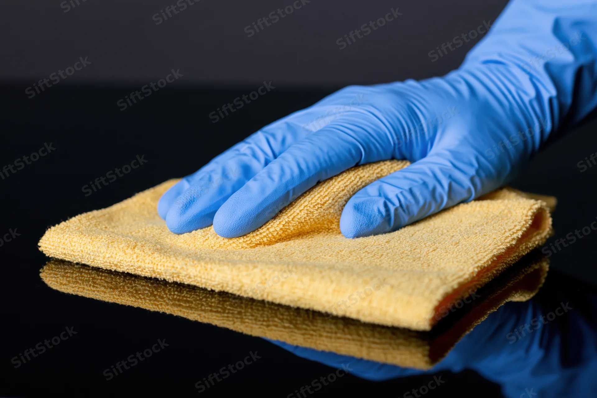 Gloved hand wiping a black reflective surface with a yellow cloth