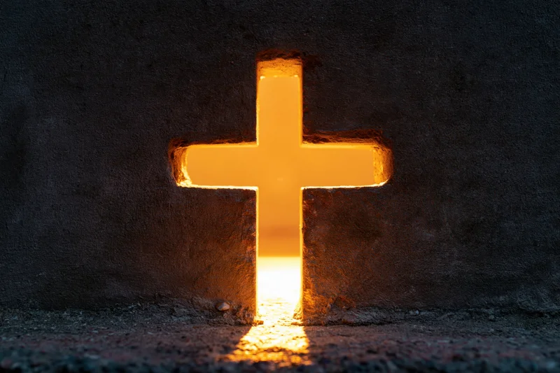 Glowing christian cross cut into dark concrete wall with warm light shining through