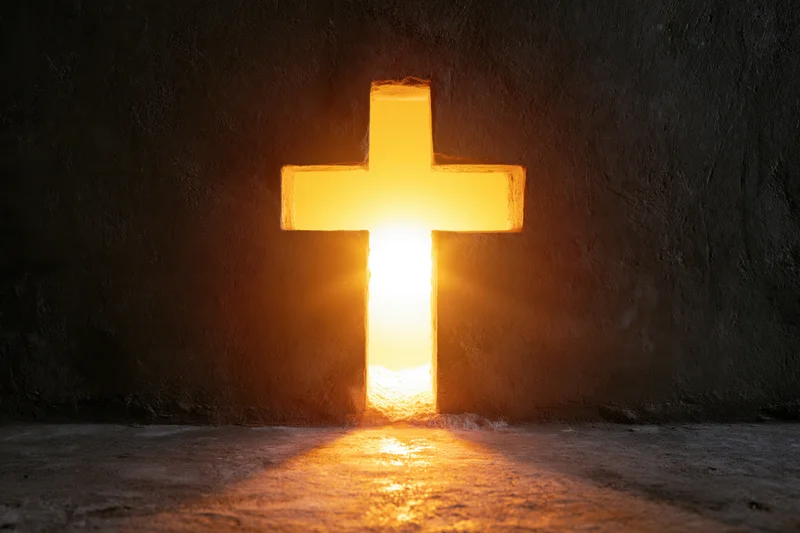 Glowing christian cross cut into dark concrete wall with warm light shining through