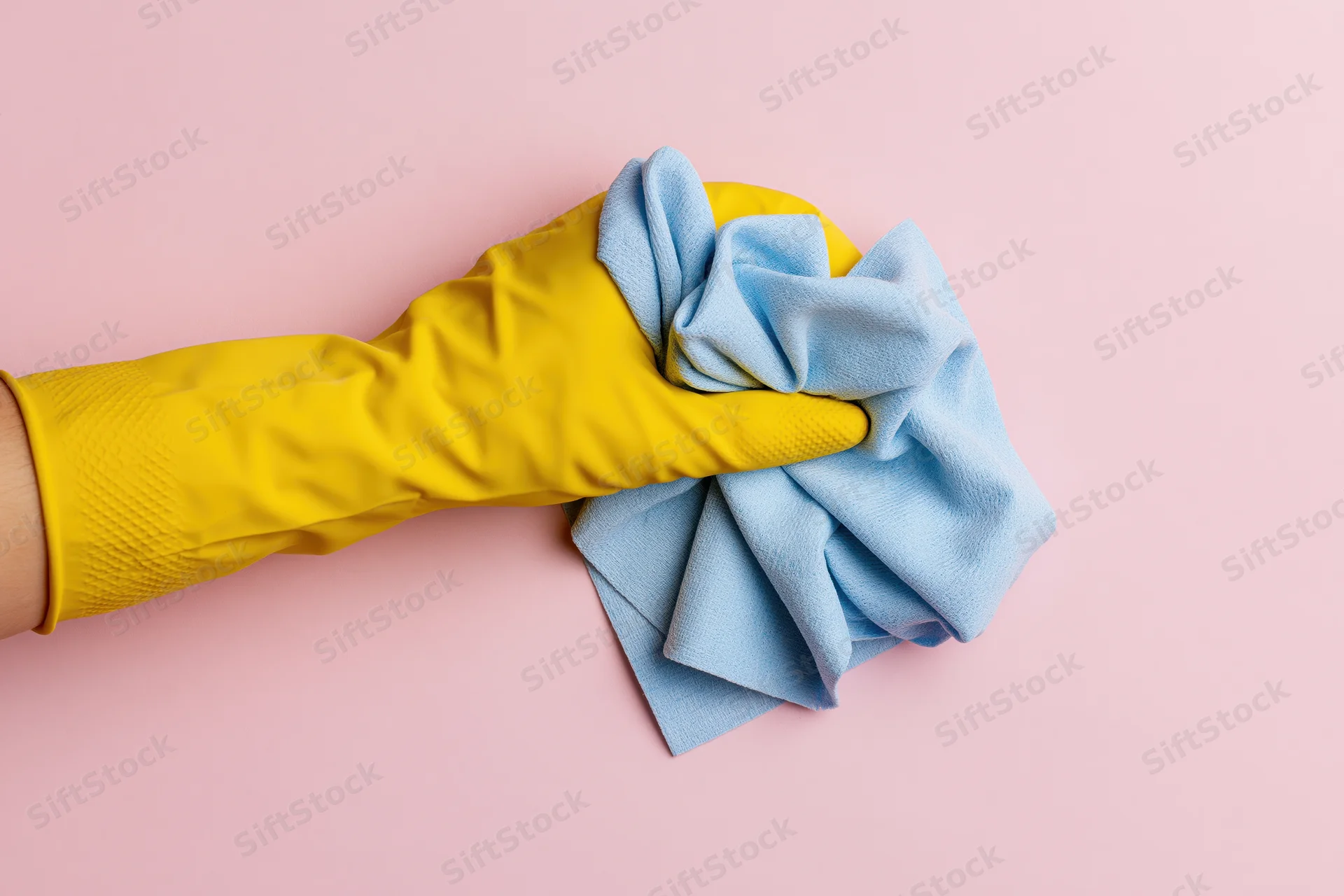 Hand in yellow rubber glove holding blue cloth against pink background