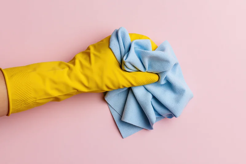 Hand in yellow rubber glove holding blue cloth against pink background