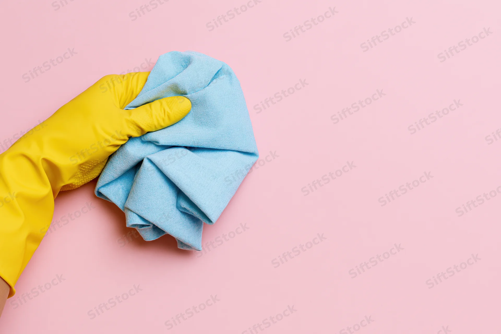 Hand in yellow rubber glove holding blue cloth on pink background