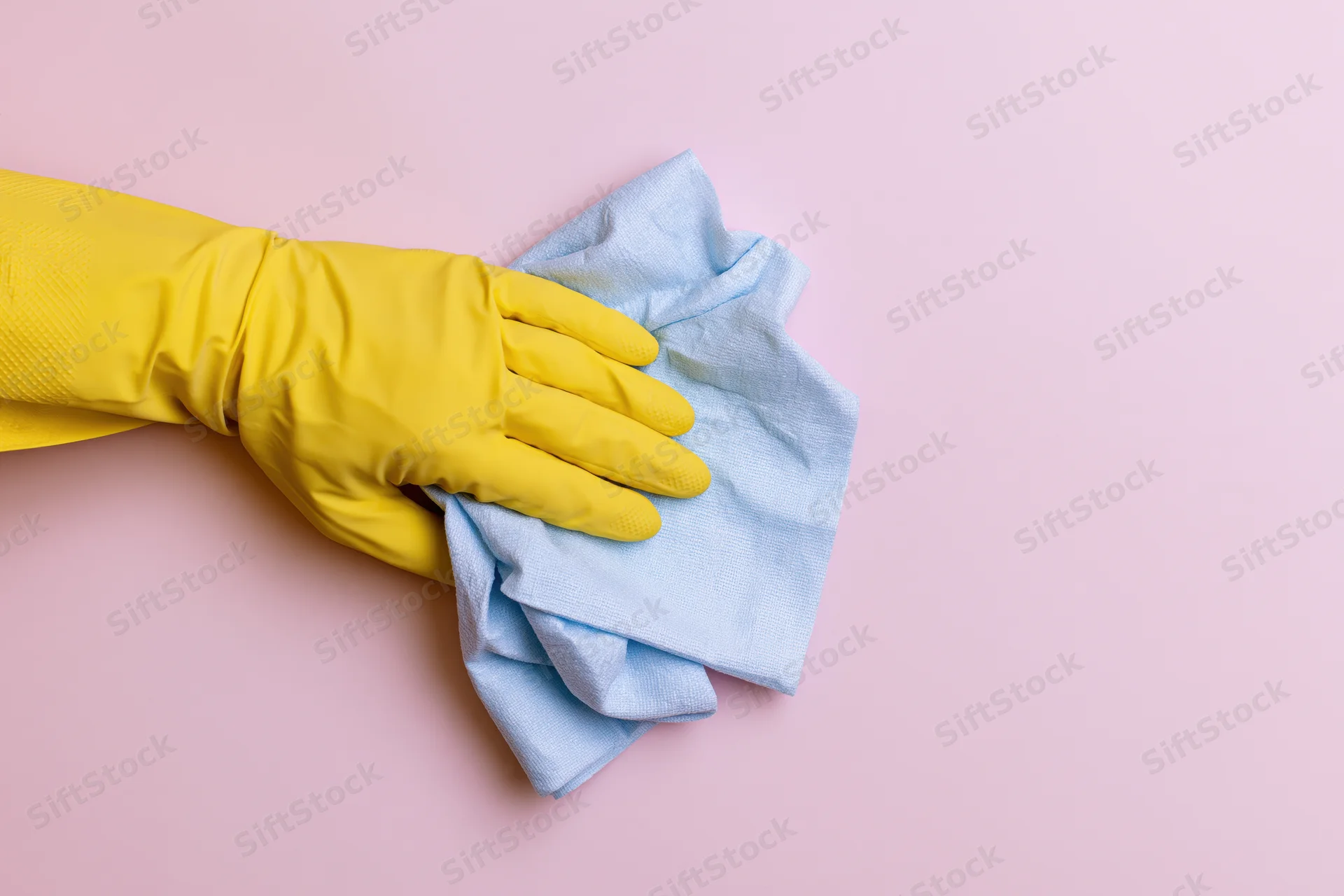 Hand in yellow rubber glove wiping a blue cloth on pink surface